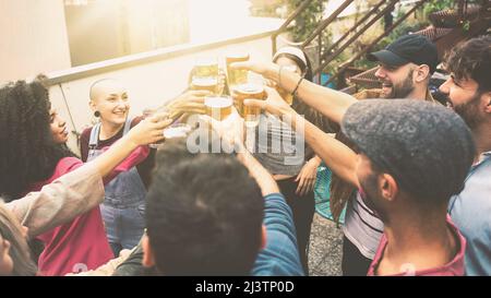 Groupe joyeux d'étudiants interraciaux en dégustant de la bière. Happy People Party dans l'auberge de jeunesse sur le toit. Image filtrée avec lumière solaire Banque D'Images