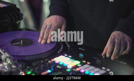 DJ mélange la musique de la télécommande. Art. Un homme règle la musique de la télécommande. Le gars avec tatouages fait tourner les boutons de la télécommande musicale Banque D'Images