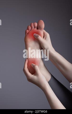 Douleur au talon et à la balle du pied. Femme tenant la jambe avec un spot rouge de près. Inflammation, port de mauvaises chaussures, blessures, posture inconvenante, arthrite, maladies chroniques. Banque D'Images