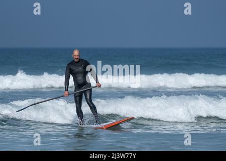Un paddle-boardeur mâle mature qui fait une vague à Fistral, à Newquay, dans les Cornouailles, au Royaume-Uni. Banque D'Images