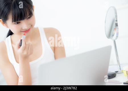 Beauté de la jeune femme asiatique avec apprendre le maquillage avec le rouge à lèvres sur la bouche regardant ordinateur portable avec tutoriel cours en ligne, l'enseignement féminin et expl Banque D'Images