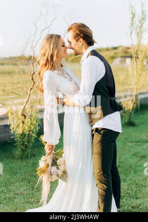 Couple élégant de jeunes mariés qui marchent sur le terrain le jour de leur mariage avec bouquet Banque D'Images