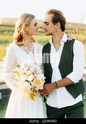 Couple élégant de jeunes mariés qui marchent sur le terrain le jour de leur mariage avec bouquet Banque D'Images