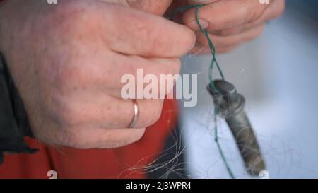 Mains mâles tenant un crochet de pêche.clip. Une vue des mains mâles fortes tenant un crochet conçu pour la pêche sur lequel il y a un long fil Banque D'Images