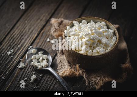 Farmers cottage fromage dans un bol en argile, à côté d'une cuillère sur fond de bois foncé, gros plan. Nourriture saine naturelle, alimentation saine Banque D'Images