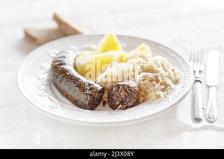 Saucisse sanglante et choucroute à la sauce avec pommes de terre cuites en gros plan. Plat slovène traditionnel avec saucisse sanglante rôtie Banque D'Images