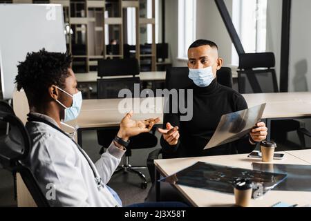 Beau patient asiatique avec une radiographie de la fracture des os du pied lors de la consultation d'un médecin noir. Chirurgien africain discutant de la radiographie avec le patient Banque D'Images