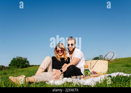 Image à angle bas d'un jeune couple heureux amoureux ayant un pique-nique sur une prairie de printemps dans une campagne. Assis sur une couverture par temps ensoleillé. Banque D'Images