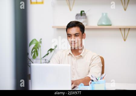 Un jeune asiatique s'assoit à son bureau et se pose sur son ordinateur portable au travail Banque D'Images