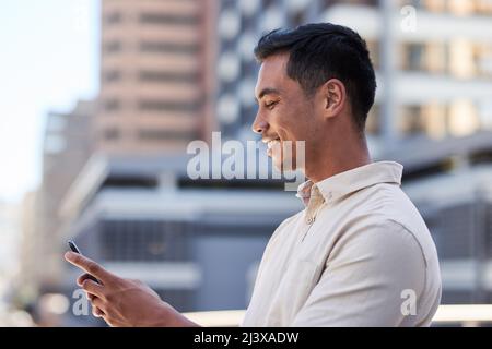 Vue latérale d'un jeune homme asiatique tapant sur son téléphone portable dans la ville Banque D'Images