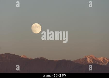 La pleine lune s'élève au-dessus de la chaîne de montagnes du ciel du soir Banque D'Images