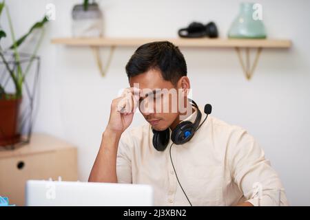 Un jeune homme d'affaires asiatique se frotte les yeux contre son bureau qui semble contrarié Banque D'Images