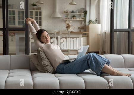 Une femme heureuse utilisatrice d'ordinateur portable se détendant sur un canapé confortable et spacieux Banque D'Images