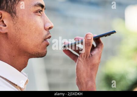 Un gros plan du jeune homme asiatique envoie une note vocale en utilisant un téléphone cellulaire en ville Banque D'Images