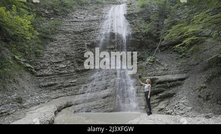 Femme prenant des photos ou filant des montagnes et des chutes d'eau sur son smartphone à l'aide d'un trépied. Action. Femme voyageur avec un bâton de selfie et un Banque D'Images