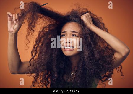 Je pensais que passer à la nature serait moins une lutte. Photo d'une femme qui pleure tout en peignant ses boucles sur un fond orange. Banque D'Images