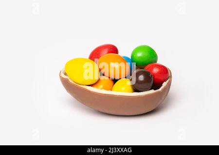 Œuf de pâques au chocolat craqué avec de petites friandises rondes colorées sur fond blanc, espace pour les copies, vue latérale. Chocolat pour les enfants. Concept de Pâques. Banque D'Images