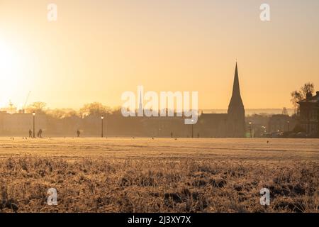 Une vue sur Blackheath Common en hiver pendant un coucher de soleil chaud. L'église de la Toussaint peut être vue au loin et les gens peuvent être vus à pied. Banque D'Images