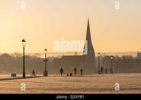 Une vue sur Blackheath Common en hiver pendant un coucher de soleil chaud. L'église de la Toussaint peut être vue au loin et les gens peuvent être vus à pied et à vélo Banque D'Images