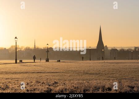 Une vue sur Blackheath Common en hiver pendant un coucher de soleil chaud. L'église de la Toussaint peut être vue au loin et les gens peuvent être vus à pied. Banque D'Images