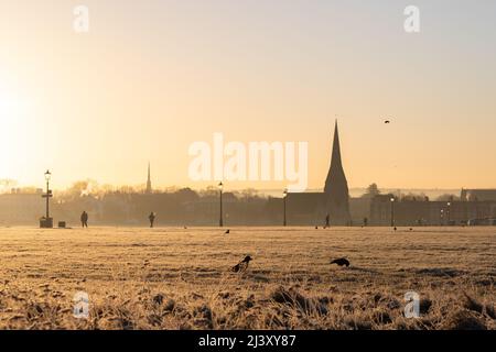 Une vue sur Blackheath Common en hiver pendant un coucher de soleil chaud. L'église de la Toussaint peut être vue au loin et les gens peuvent être vus à pied. Banque D'Images