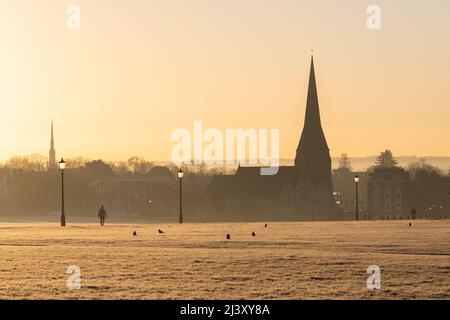 Une vue sur Blackheath Common en hiver pendant un coucher de soleil chaud. L'église de la Toussaint peut être vue au loin et les gens peuvent être vus à pied. Banque D'Images