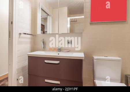 Salle de bains avec armoire en bois marron, lavabo en résine blanche et armoire avec miroir au-dessus de l'évier Banque D'Images