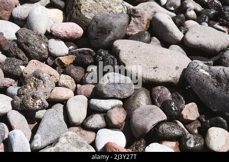 Pierres humides et sèches baignées par la lumière du soleil sur la plage. Différentes formes et tailles de texture de cailloux délavés arrière-plan Banque D'Images