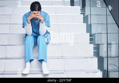 Traiter les malades n'est pas facile et les perdre est encore plus difficile. Photo d'une infirmière qui regarde stressée tout en étant assise sur un escalier. Banque D'Images