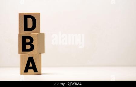 DBA - acronyme de blocs de bois avec des lettres, administrateur de base de données ou faisant des affaires comme concept d'abréviation DBA, lettres aléatoires autour, fond gris Banque D'Images