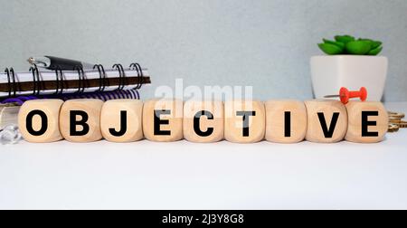 Le mot OBJECTIF se compose de blocs de construction en bois reposant sur une table sur un fond blanc à côté d'un stylo, d'un bloc-notes, d'une calculatrice. Concept Banque D'Images