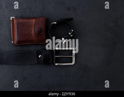 Accessoires pour hommes STILL Life avec montre, portefeuille en cuir et ceinture sur une table sombre. Ensemble d'accessoires pour hommes pour l'entreprise. Banque D'Images