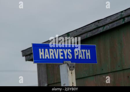 Un panneau de nom de rue en métal bleu est fixé à un poteau carré en bois blanc. Le texte blanc sur le signe indique Harvey's Path en majuscules. Banque D'Images