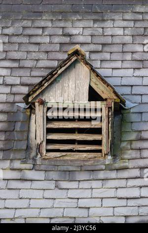 Un toit en tuiles grises sur une matinée givrée avec un ancien évent d'air négligé avec des persiennes en bois en décomposition et des signes de ver à bois Banque D'Images