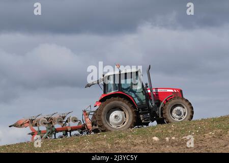 Un tracteur rouge Massey Ferguson 5470 labourage en montée dans un champ de récolte par une journée ensoleillée Banque D'Images