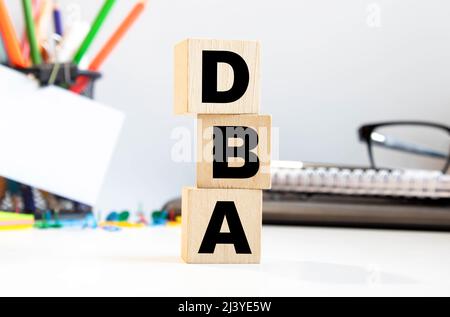 DBA - acronyme de blocs de bois avec des lettres, administrateur de base de données ou faisant des affaires comme concept d'abréviation DBA, lettres aléatoires autour, fond gris Banque D'Images