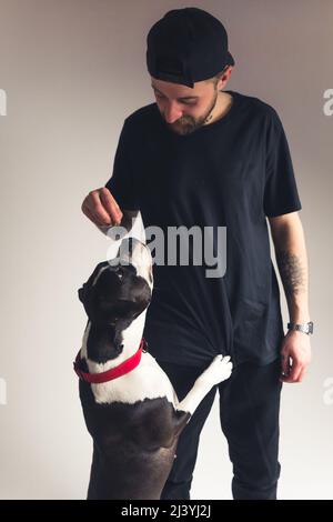 Photo en studio verticale d'un homme propriétaire de chien vêque de vêtements noirs donnant des friandises pour chien à son meilleur ami animal. Photo de haute qualité Banque D'Images