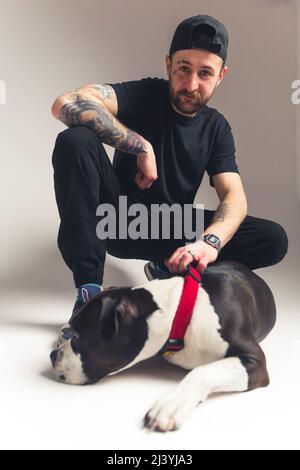 Bon garçon. Concept de dressage de chiens. Gangster-comme caucasien tatoué homme barbu tenant son grand chien par collier rouge. . Photo de haute qualité Banque D'Images