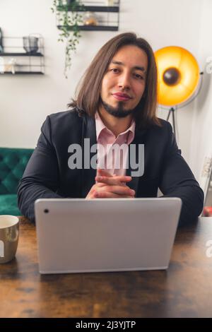 Jeune homme souriant aux cheveux sombres assis près de la table et ordinateur portable de travail à distance concept . Photo de haute qualité Banque D'Images