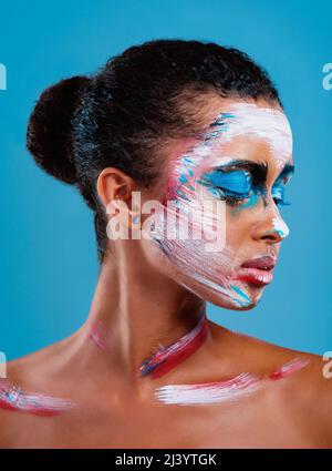 Mettez toujours votre meilleur côté vers l'avant. Photo studio d'une belle jeune femme couverte de peinture sur le visage posant sur un fond bleu. Banque D'Images