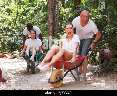 Les hommes conduisent leurs filles dans les brouettes de jardin. Funny parc d'amusement park Banque D'Images