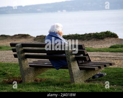 Personne âgée assise sur un banc donnant sur la mer à New Milton, Hampshire Banque D'Images