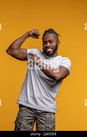 Souriant heureux mignon athlétique Africain américain mâle pointant vers son biceps sur le haut du bras Banque D'Images