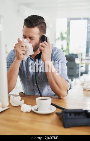 Le froid l'a laissé se sentir assez congestionné. Petit cliché d'un jeune homme d'affaires soufflant le nez tout en parlant au téléphone dans un bureau. Banque D'Images