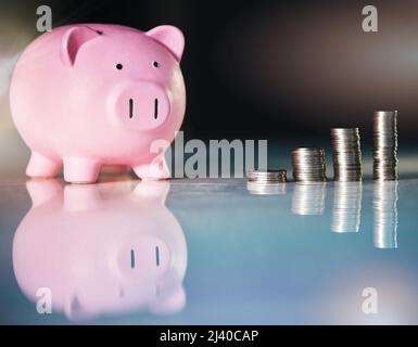 Un peu d'économies va beaucoup. Coup de pigegibank et de pièces empilées sur un bureau dans un bureau vide. Banque D'Images