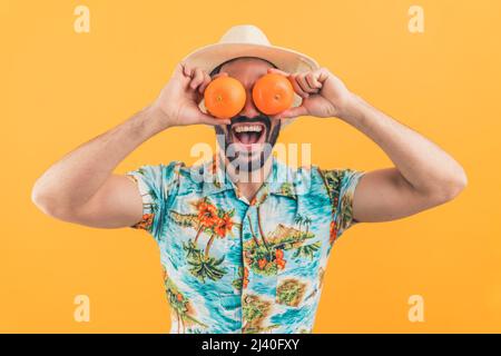 Jeune barbu homme attrayant tenant des oranges devant ses yeux sur le fond orange. Émotions folles, prise de vue en studio. Photo de haute qualité Banque D'Images