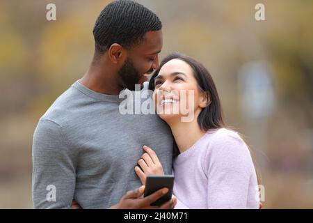 Un couple heureux tenant un smartphone se regardant l'un l'autre amoureux dans un parc Banque D'Images