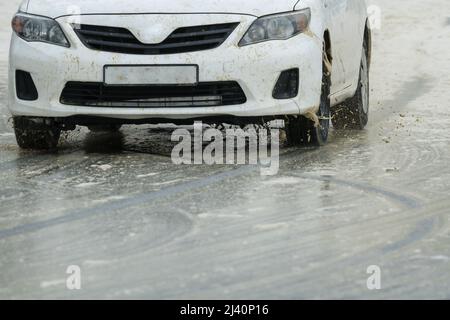 gros plan d'une voiture blanche roues avant roulant sur une route glissante et humide pendant un concept d'hiver temps et sécurité routière Banque D'Images