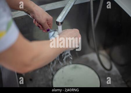 Une femme lave la vaisselle sous un jet d'eau. Détails de la cuisine. Lave-vaisselle nettoie la cuillère dans l'évier. L'eau chaude de fond coule du robinet. Banque D'Images