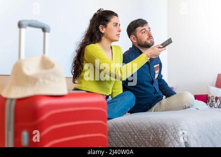 Un jeune couple de touristes regardant la télévision dans une chambre d'hôtel Banque D'Images